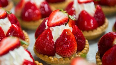 Close-up of strawberry tarts from Les Halles Boulangerie-Patisserie, featuring fresh strawberries, whipped cream, and a golden pastry base, all arranged closely together on a tray.