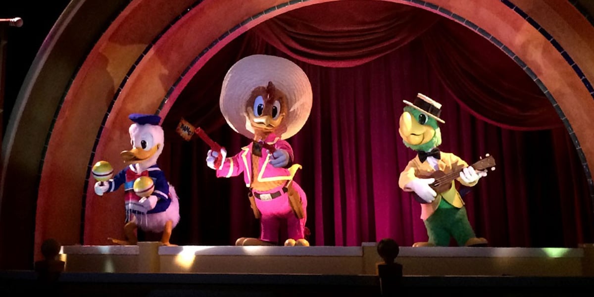 Three colorful animatronic characters—Donald Duck with maracas, José Carioca with a guitar, and Panchito Pistoles in a sombrero—stand on stage under a decorative arch with red curtains, delighting fans amid recent Walt Disney World rumors.