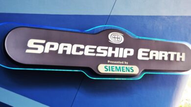 A sign reads “Spaceship Earth presented by Siemens” with a globe icon above the text, mounted on a blue wall.