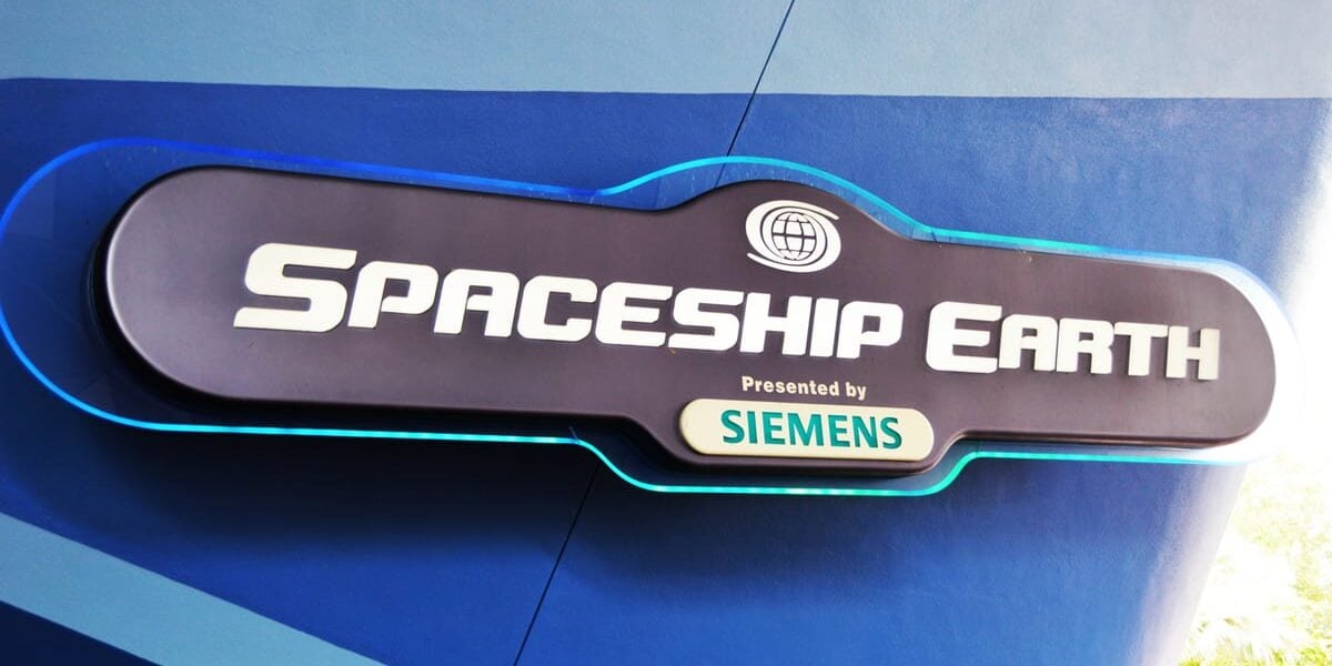 A sign reads “Spaceship Earth presented by Siemens” with a globe icon above the text, mounted on a blue wall.