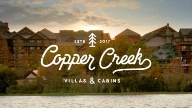 A scenic view of Copper Creek Villas & Cabins at sunset. The foreground features a serene lake, with lush trees and rustic buildings in the background. The establishment year, 2017, is noted with the logo.