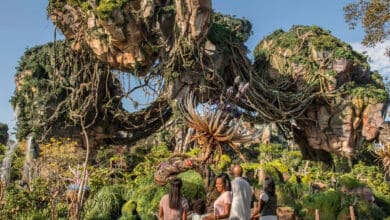 A group of people stand in a lush, fantastical landscape with floating mountains and alien plants beneath a clear blue sky, reminiscent of Pandora – The World of Avatar.