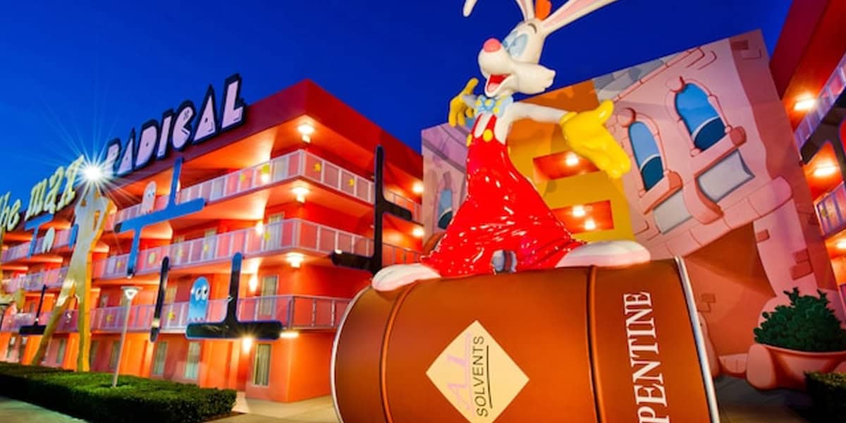 A large Roger Rabbit statue in red overalls stands on a paint can in front of a brightly colored, cartoon-themed hotel building at dusk, perfect for a memorable photo during your Pop Century Resort Review.