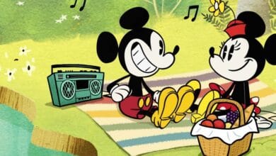 Mickey Mouse and Minnie Mouse sit on a striped picnic blanket by a pond, sharing bananas and fruit from a basket during their Picnic at Disney World, with a radio playing music and musical notes floating in the air.