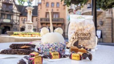 A table displays a white chocolate-covered caramel apple with sprinkles, Werther’s Original caramel popcorn, chocolates, and brownies.