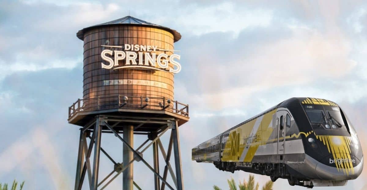 A sleek Brightline train travels past a large, rustic water tower with "Disney Springs" written on it. The sky is mostly cloudy, creating a backdrop that highlights the scene at Disney World thanks to the DeSantis Disney district.