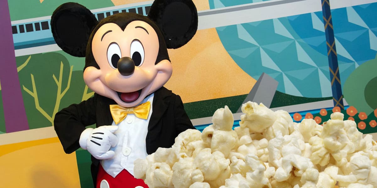 Mickey Mouse in a tuxedo with a yellow bow tie stands next to a large pile of popcorn, with a colorful geometric mural and hints of iconic Disney scents in the background.