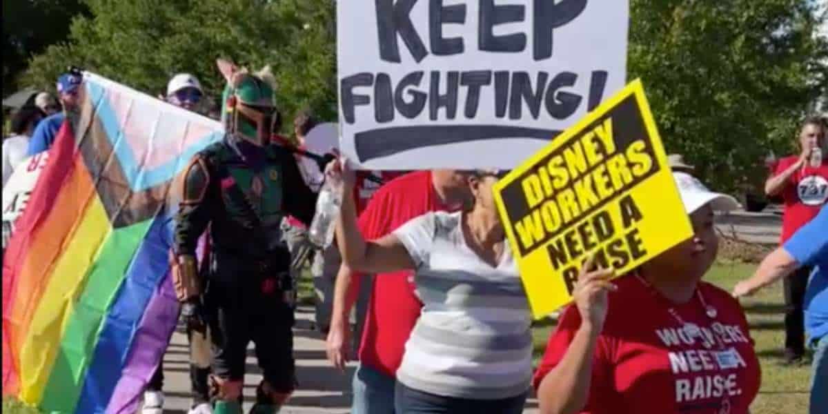 737 protestors hold signs saying disney workers deserve a raise and pride flags while a man dressed as the mandalorian joins them