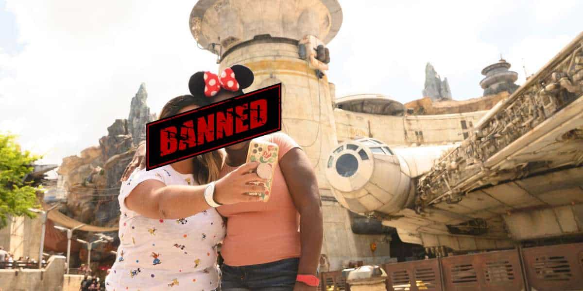 two women in mickey ears take a selfie in front of galaxys edge at disney with text reading BANNED in red and black over their faces