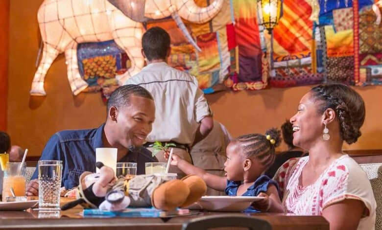 A family of three smiles and enjoys a meal together at a restaurant with colorful decor, including a large patchwork animal sculpture on the wall behind them, made possible by easy dining reservations. The child reaches for food while parents watch affectionately.