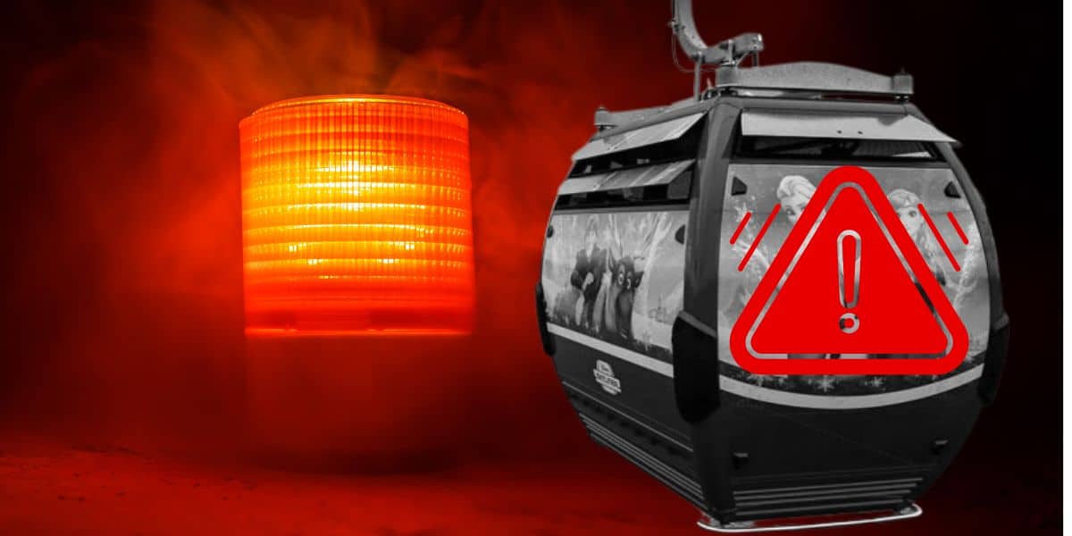 A red emergency light flashes next to a gondola lift resembling the Disney Skyliner, which bears an exclamation mark warning sign. The background is dark and smoky, heightening the sense of urgency in the scene.
