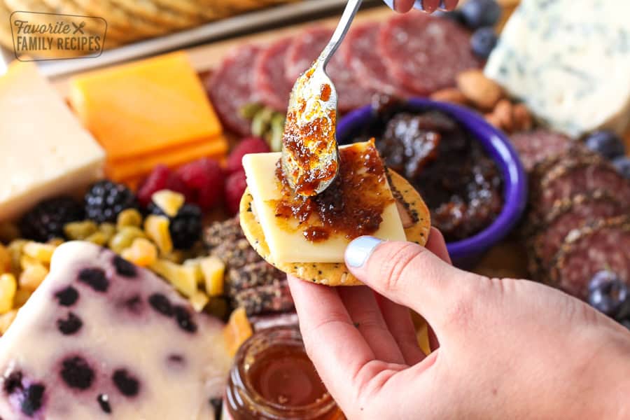 A cracker with cheese and jam being spooned on it.