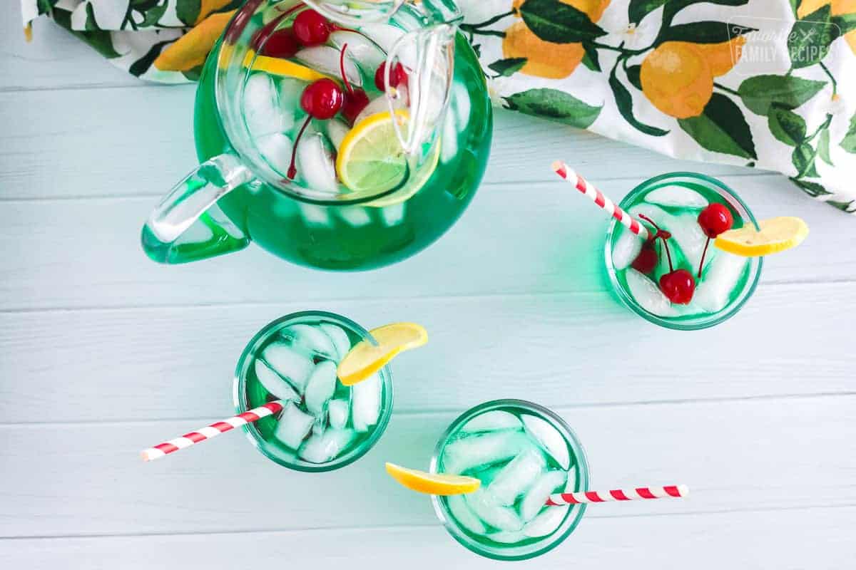 Three cups and a pitcher of mint juleps with cherries and lemon slices