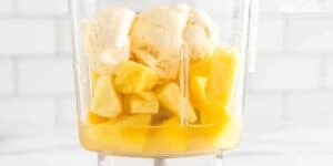 A blender filled with vanilla ice cream and sliced bananas, ready for blending. the background is a bright, clean kitchen setting.