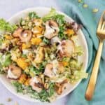 A colorful salad with chicken, greens, nuts, and fruits on a white plate beside a gold fork, on a teal napkin. the upper left corner has a "favorite family recipes" logo.