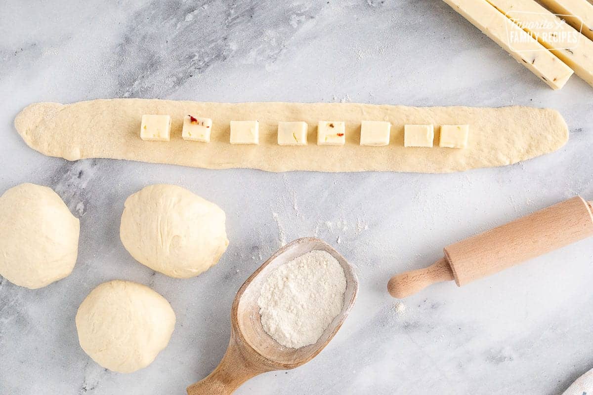 Long flattened piece of dough with cheese cubes lined up in the center.