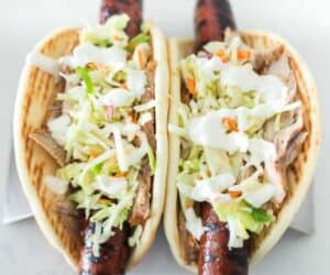 Two grilled sausages in buns topped with shredded coleslaw on a white plate, inspired by the Ronto Wrap recipe.