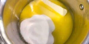 A stainless steel bowl containing melted butter, a pool of beaten egg, and a mound of granulated sugar, ingredients combined for a baking recipe.