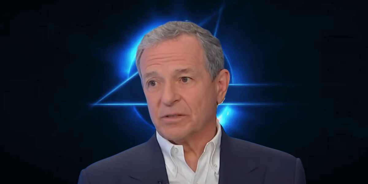 Bob Iger, with a serious expression, wearing a light blue shirt against a dark background with a blue geometric light pattern.