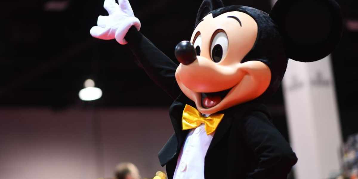 Mickey Mouse, a Disney character in a tuxedo and gloves, cheerfully waving at an event.