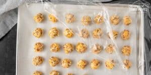 Rows of raw cookie dough balls on a parchment-lined baking tray, ready to be baked into fried biscuits.