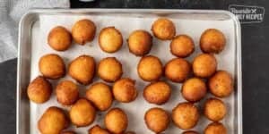 A tray of golden-brown hush puppies arranged neatly on a baking sheet lined with parchment paper, viewed from above, ready for the fried biscuits recipe.