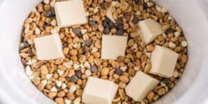A white bowl is filled with a mixture of caramel, white, and semi-sweet chocolate chips. Six large squares of white chocolate or similar confectionery are evenly placed on top of the mixture. The bowl's contents are arranged to cover the bottom evenly.
