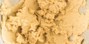 A close-up view of unbaked cookie dough. The dough has a light beige color and a creamy, slightly crumbly texture.