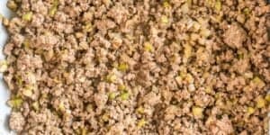 Cooked ground beef mixed with diced onions and green bell peppers, spread evenly across a surface, showcasing the texture and ingredients. The beef is browned, and the vegetables are softened, blending well together.