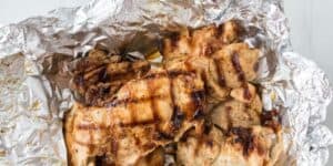 Grilled chicken pieces with char marks placed on a sheet of crinkled aluminum foil.