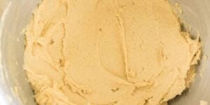 A close-up shot of a mixing bowl filled with creamy, beige-colored cookie dough. The dough appears to be smooth and evenly mixed, likely ready for baking. The edges of the metal bowl are slightly visible.
