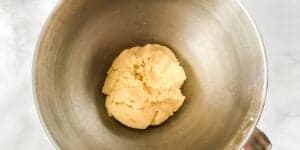 A stainless steel mixing bowl containing a ball of unbaked cookie dough, resting on a white countertop.
