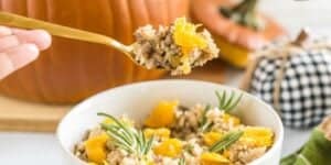 A close-up of a person holding a spoonful of rice mixed with chopped vegetables and herbs. Below, a white bowl is filled with the same rice mixture, garnished with rosemary sprigs. In the background, there are two pumpkins, one plain and one with a checkered pattern.