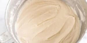 A metal mixing bowl filled with smooth, light beige batter. The sides of the bowl have some remnants of flour, indicating that the mixture has been thoroughly blended.