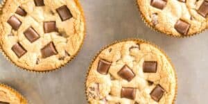 Chocolate chip muffins with chunks of chocolate on top, displayed on a metal baking sheet.