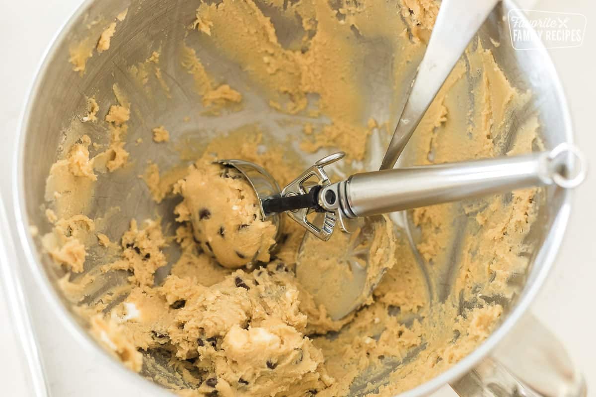 A bowl of cookie dough with an ice cream scoop in it.