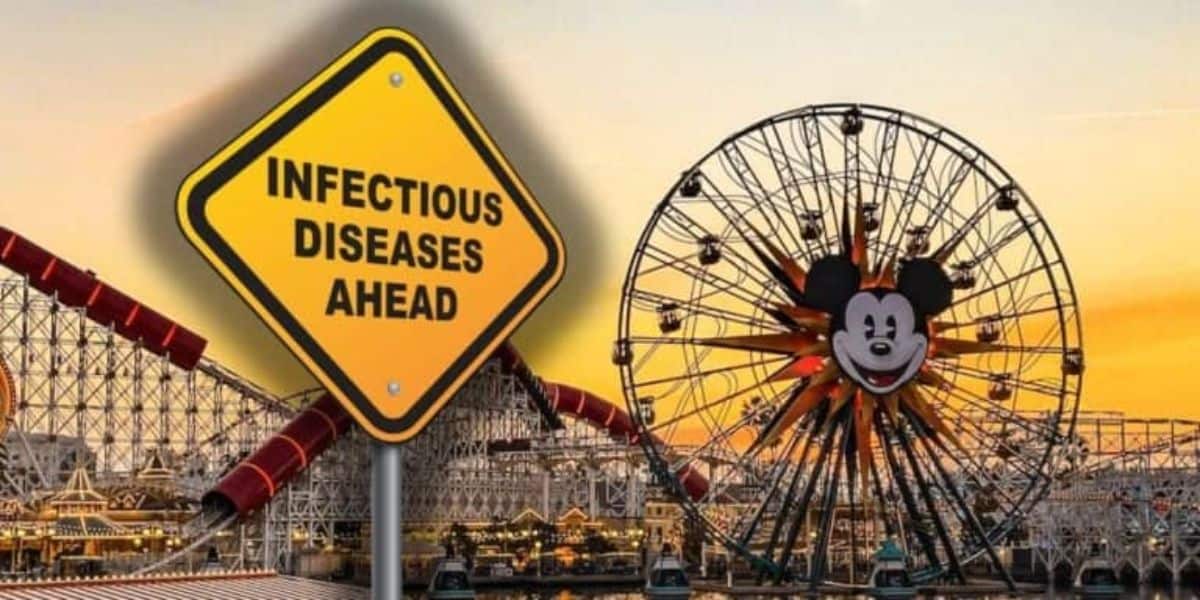 A yellow sign reading "Infectious Disease Ahead" in front of Disneyland in California as the sun sets in the background.