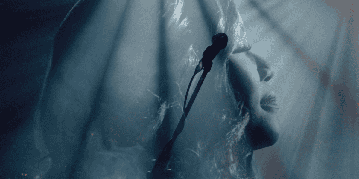 Silhouette of a person singing into a microphone against a background of ethereal light rays. The image is double-exposed, showing close-up facial features with eyes closed, creating a serene and contemplative mood.