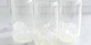 Three clear glass jars partially filled with ice cubes and a small amount of white liquid are set on a white surface with a blurred white tile background.