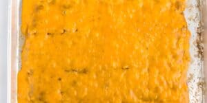 A close-up view of a baking dish filled with a cheesy casserole. The top layer is covered in melted, golden brown cheese. Edges of the dish show a slight browning where the cheese has crisped.