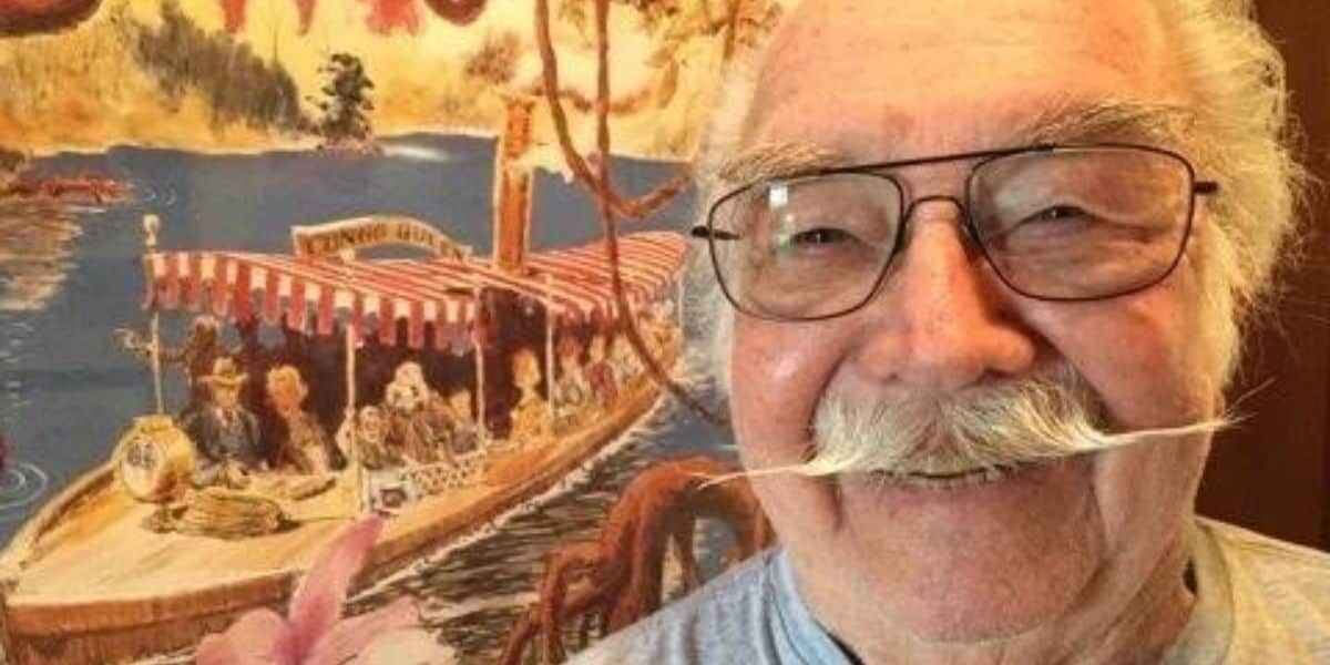 Disney Legend Bill Sullivan poses in front of a painting of The Jungle Cruise
