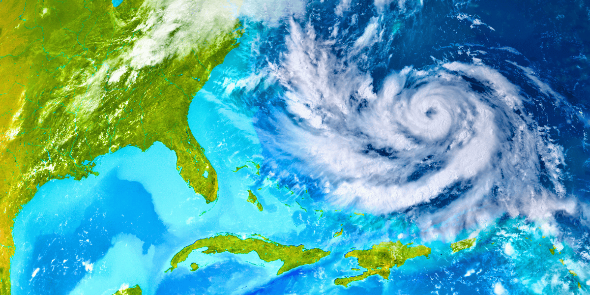 A satellite image shows a large hurricane swirling over the Atlantic Ocean, near the southeastern coast of the United States. The storm's eye is clearly visible, with spiraling cloud patterns extending outward over the Caribbean and parts of Florida.