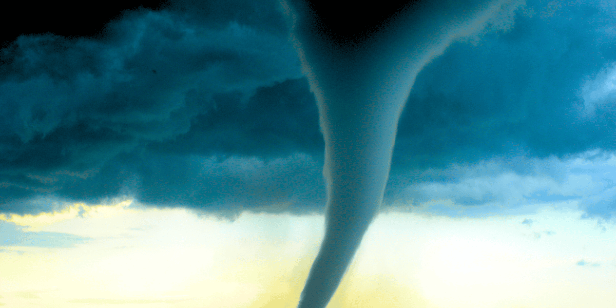 A powerful tornado extends from a dark, ominous cloud above, stretching down towards the ground. The sky around the tornado is a mix of dark blues and lighter tones, indicating a severe weather event. The funnel appears in motion against the dramatic backdrop. Disney World Tornado Watch