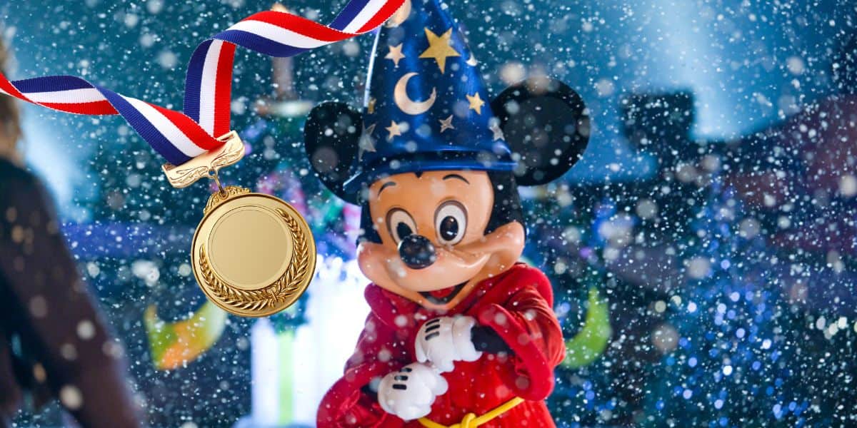 An animated character wearing a red robe and a blue wizard hat with stars stands in a snowy scene. A gold medal with a red, white, and blue ribbon floats in the upper left corner of the image.