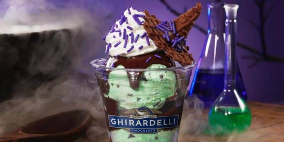 A Ghirardelli ice cream sundae featuring mint chip ice cream with green food dye, topped with whipped cream, a drizzle of chocolate sauce, purple sprinkles, and a upside-down chocolate-dipped waffle cone piece, placed amidst a misty background with lab beakers.
