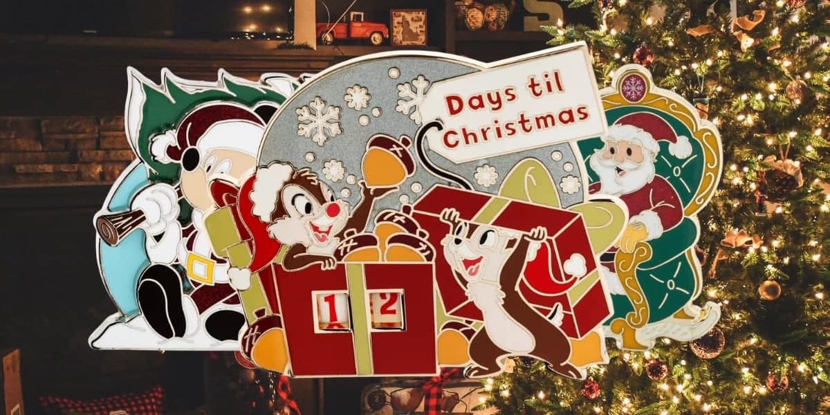 A festive scene showing cartoon characters with winter attire around a calendar. The calendar reads "Days til Christmas" with countdown numbers. A decorated Christmas tree is in the background, lit with colorful lights.