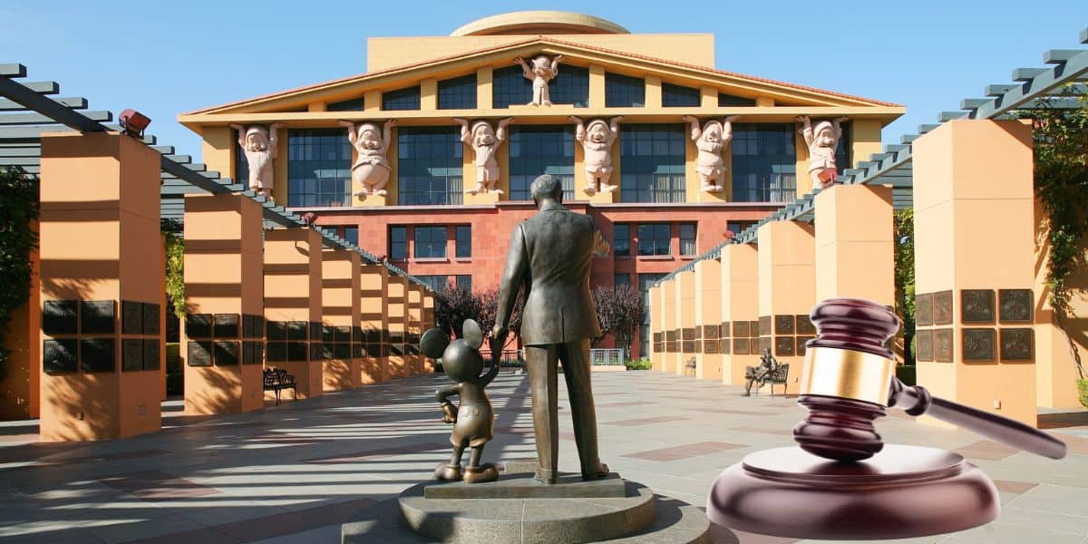 A large building with unique sculptures on the facade. In front, a statue of a man and a mouse character stands on a walkway. A judge's gavel is superimposed on the image, symbolizing legal proceedings.