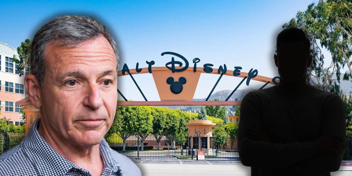 Current Disney CEO Bob Iger stands in front of the Walt Disney Studios entrance gate, featuring the iconic Mickey Mouse symbol. A shadowy figure with crossed arms is to the right. Trees and a clear sky are visible in the background.