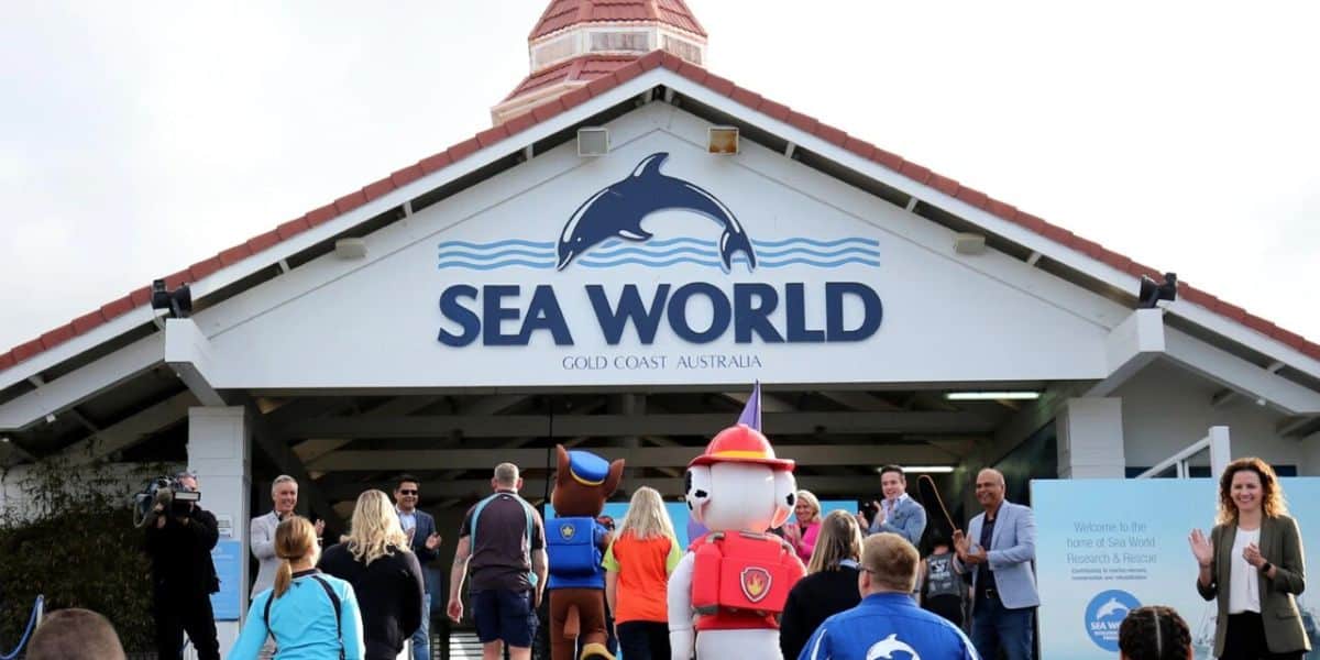 People entering Sea World Gold Coast, Australia. The entrance is decorated with a dolphin logo. Some attendees are dressed in colorful costumes.