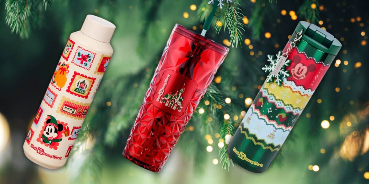 Three colorful holiday-themed Starbucks cups and tumblers are displayed against a backdrop of evergreen branches. The designs feature festive patterns, including a Mickey Mouse motif, red and green colors, and snowflakes.